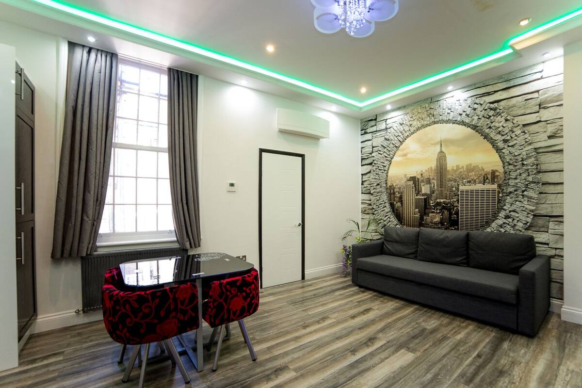 A modern living room with a stone wall mural, a black sofa, a dining table with red chairs, and a window with curtains.