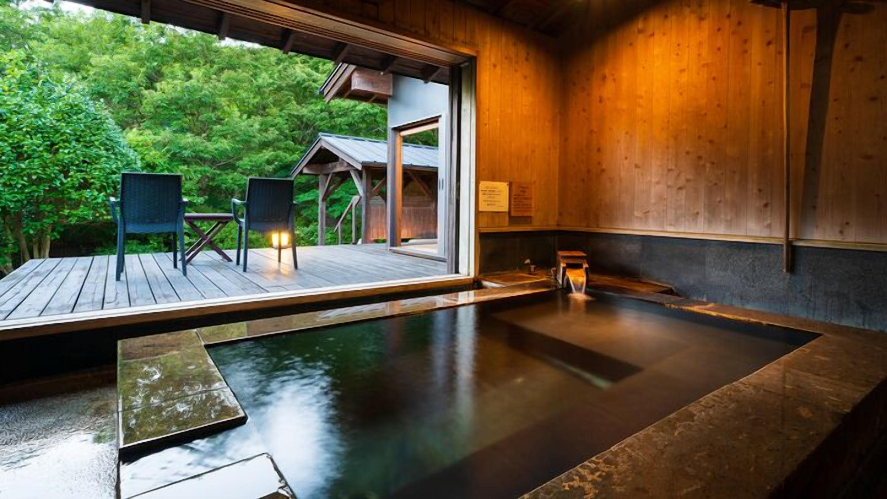 A hot spring bath area with a wooden deck, two chairs, and a small table.