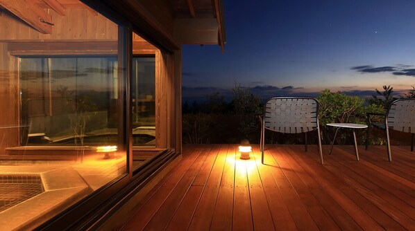 An outdoor wooden deck with two chairs and a table, a lit candle, and a view of the sky. - Spa Greenness (Kokonoe)