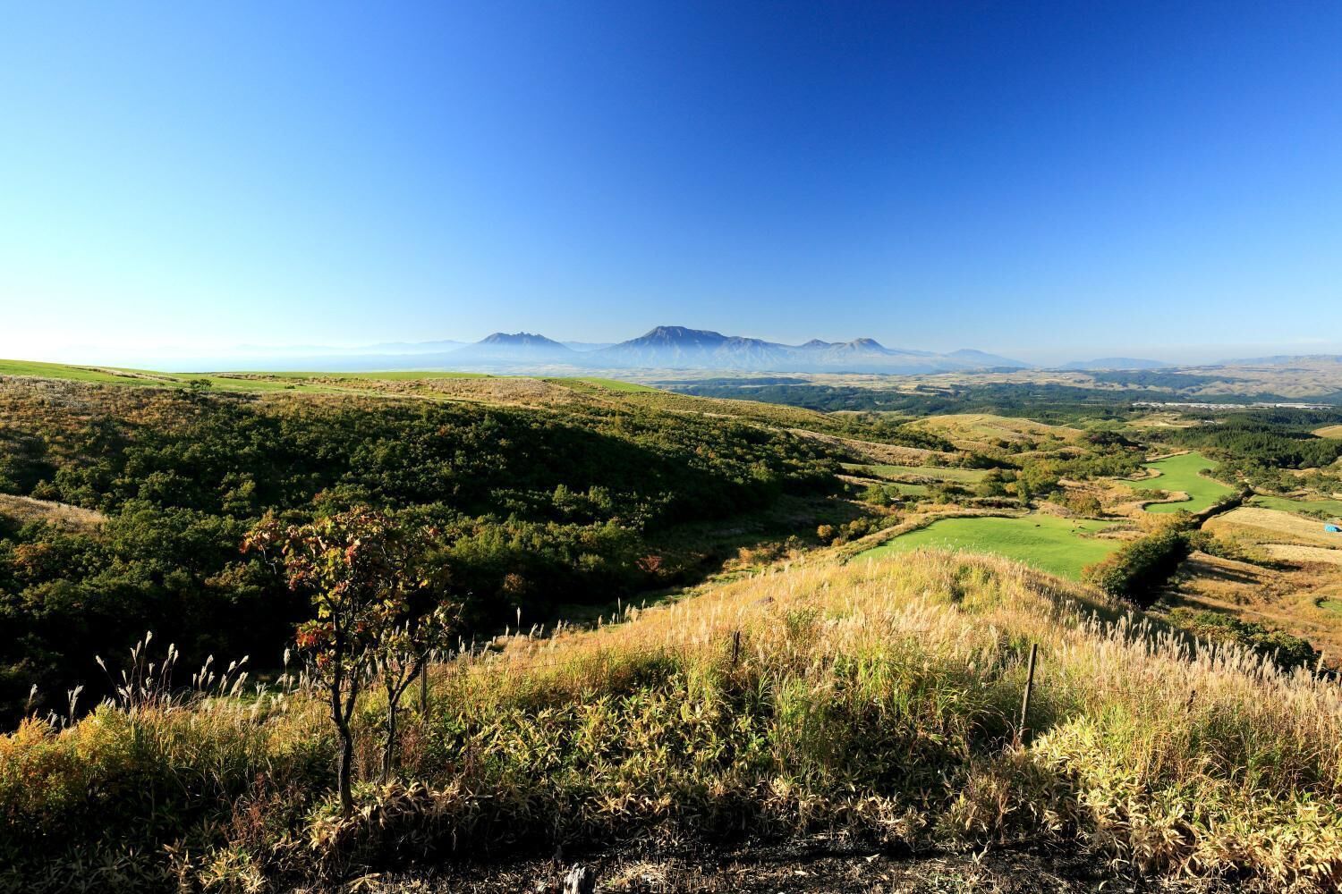 Vista panorámica de un paisaje montañoso con cielo despejado, que muestra colinas ondulantes, un valle y montañas distantes.