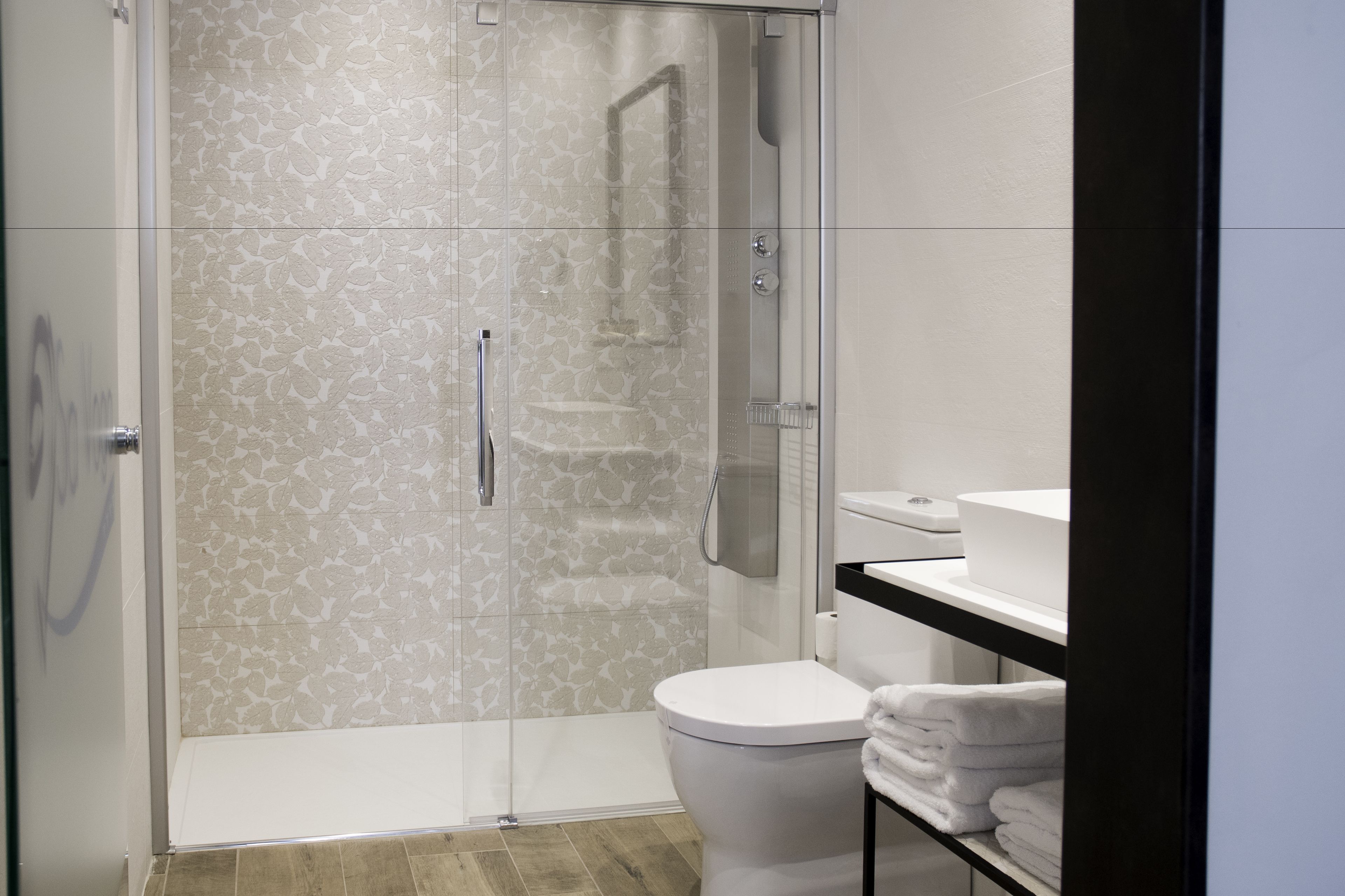 Un baño moderno con ducha de vidrio, inodoro blanco y lavamanos con encimera negra.