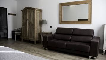 A bedroom with a wooden wardrobe, a dark brown sofa, a bedside table with a lamp, and a large mirror on the wall.