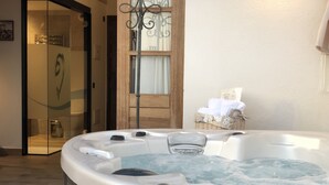 Un jacuzzi con revestimiento de madera, una puerta de vidrio que da a una zona de ducha y una cesta de mimbre con toallas en la pared.