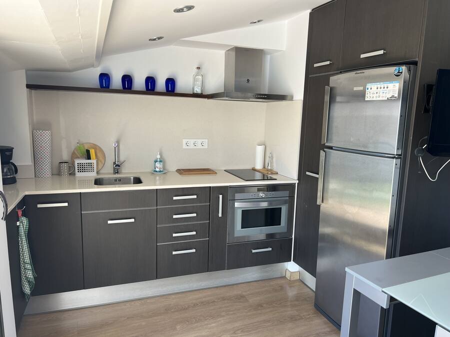 Een moderne keuken met donkere kastjes, een roestvrijstalen koelkast, een inbouwoven en een aanrecht met een koffiezetapparaat en keukengerei.