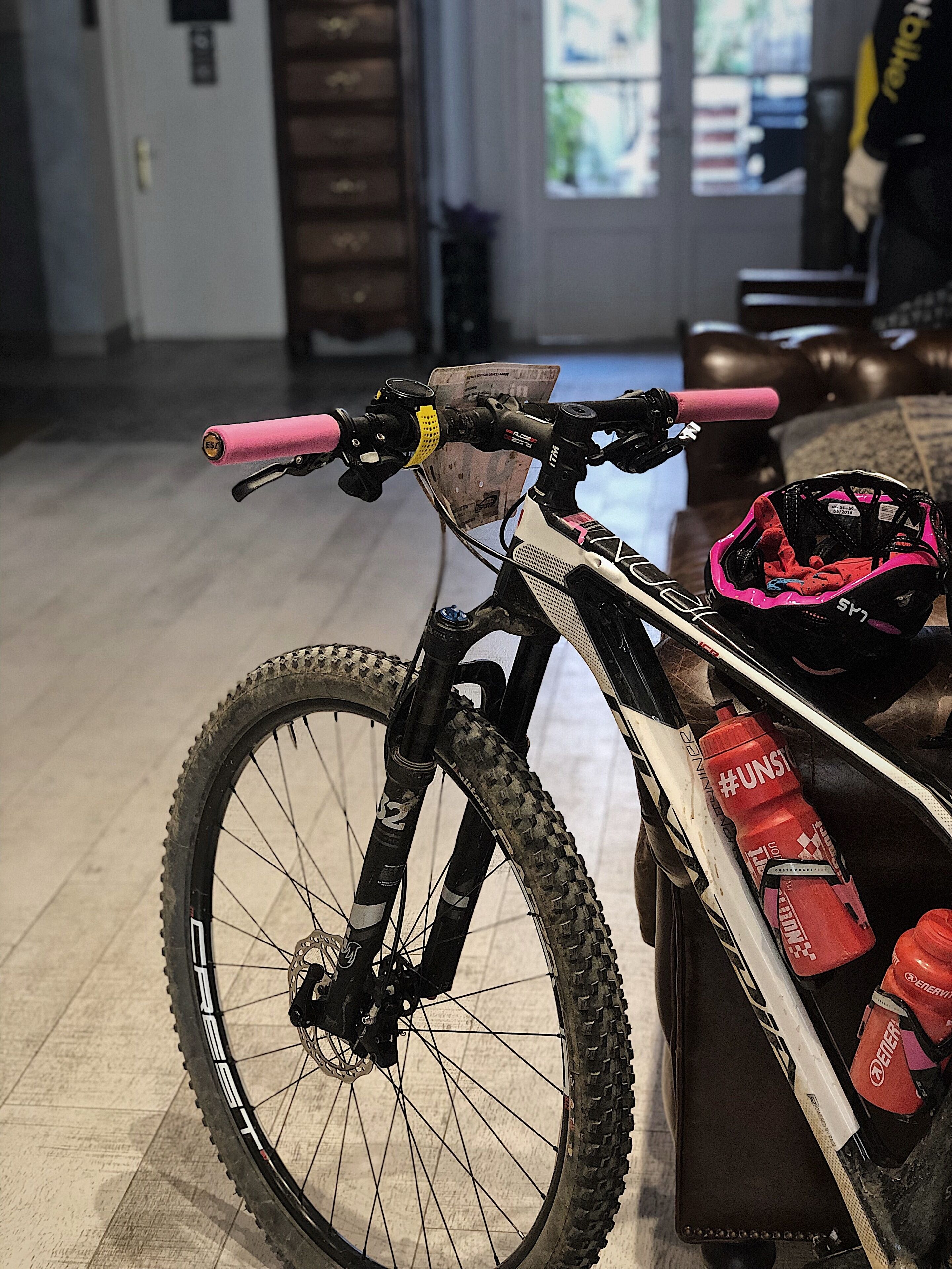 A mountain bike with a pink handlebar and a helmet on the floor.