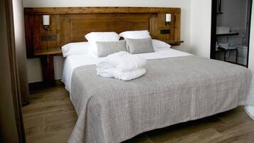 Ein ordentlich bezogenes Bett mit grauer Decke und weißen Kissen, ein hölzernes Kopfteil und ein Nachttisch mit Lampe.