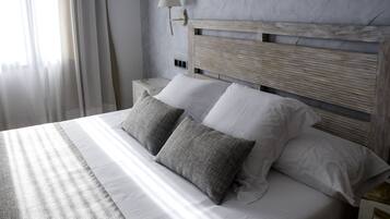 Una cama con cabecera de madera, dos almohadas blancas y una almohada gris con textura.