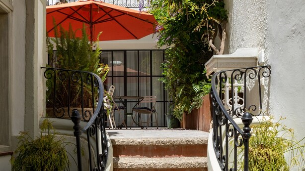 Una escalera con un paraguas rojo, plantas en macetas y un muro de ladrillo al fondo.