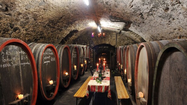 A wine cellar with wooden barrels, a central table with candles, and benches. - Hotel Weinhaus Selmigkeit (Bingen am Rhein)