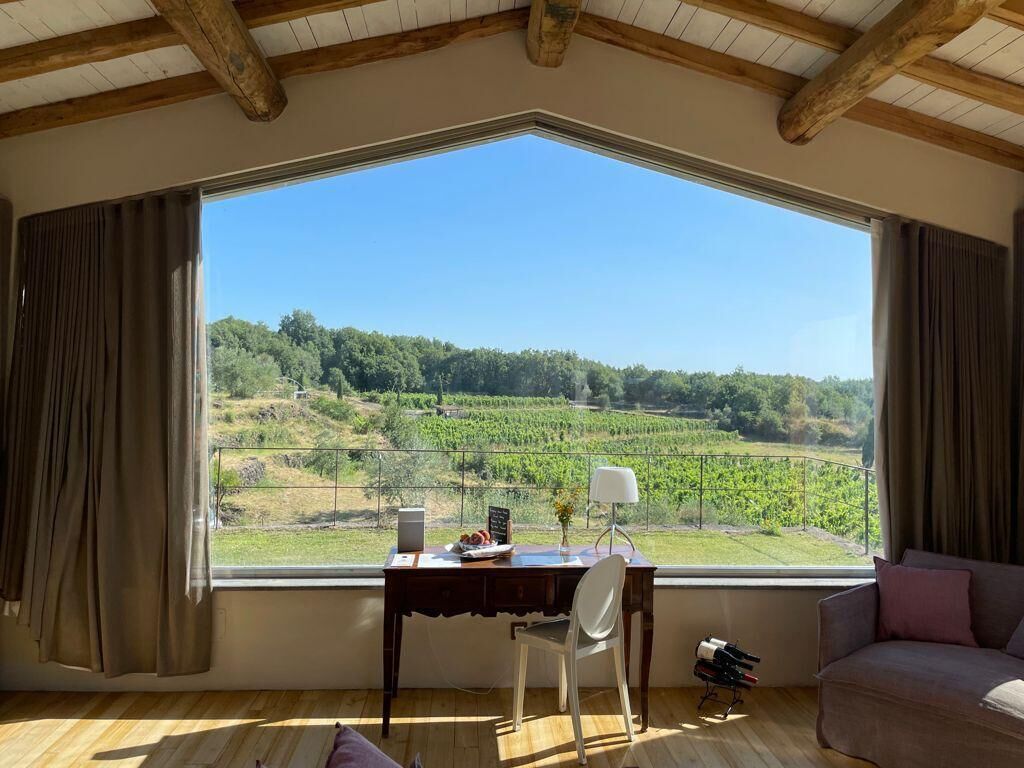 A room with a large window, a desk with a chair, a sofa, and a wine rack.
