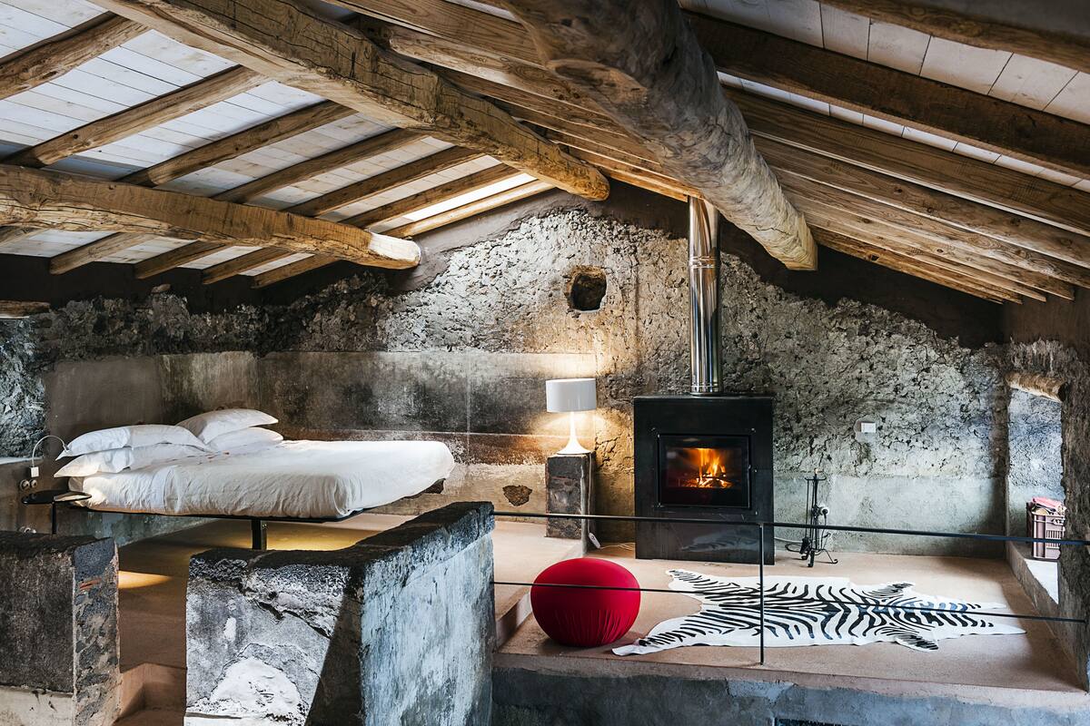 Une pièce rustique avec un mur en pierre, un lit, une cheminée et un tapis à motifs zébrés.