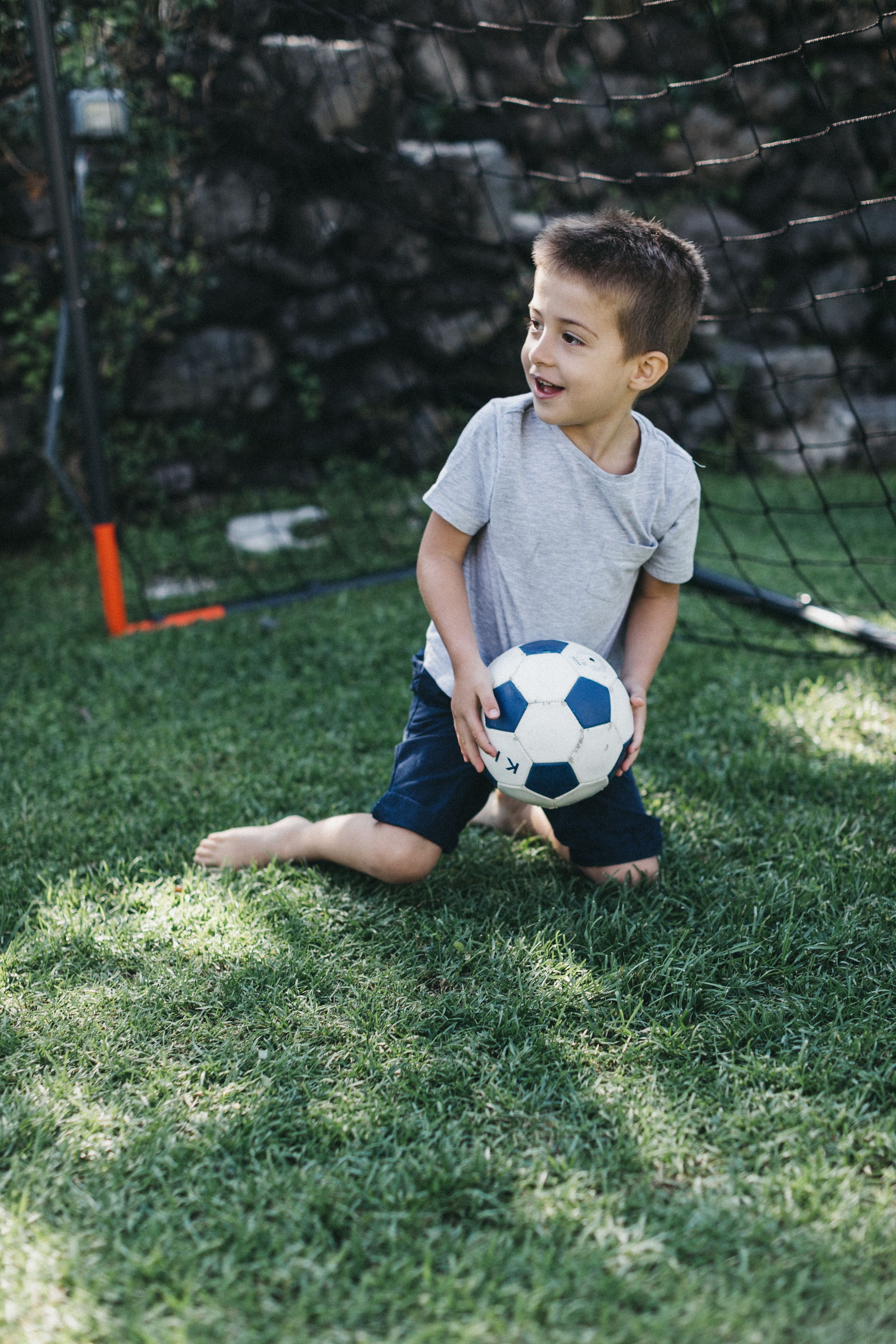 A child holding a soccer ball in a grassy area with a net in the background.