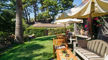 Eine Terrasse mit Holztisch, Stühlen und einer Couch unter einem großen Sonnenschirm.