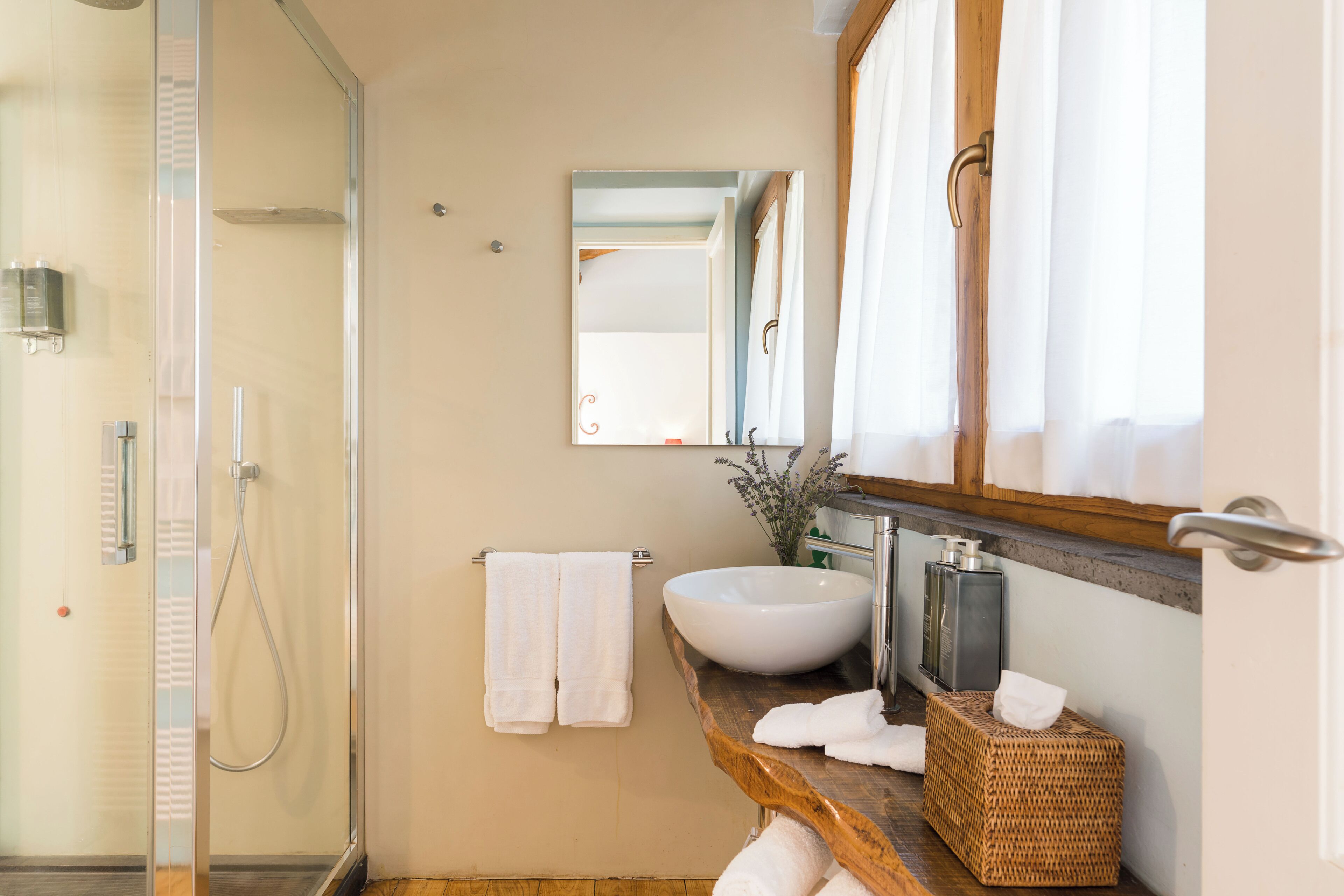 A bathroom with a glass shower enclosure, a large vessel sink, a mirror, and a wooden vanity.