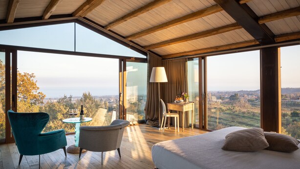 Un dormitorio con una cama grande, un escritorio y una silla, con vistas al campo a través de ventanas amplias.