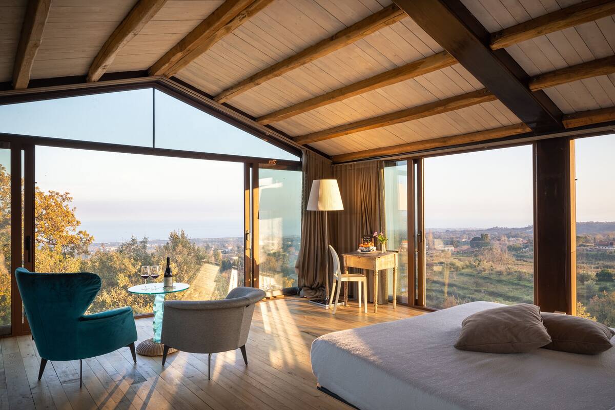 Une chambre dotée d’un grand lit, d’un bureau et d’une chaise, et offrant une vue sur la campagne grâce à de grandes fenêtres.