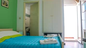Une chambre à coucher avec un lit, une armoire, une salle de bain visible à travers une porte ouverte et une vue sur l’extérieur.