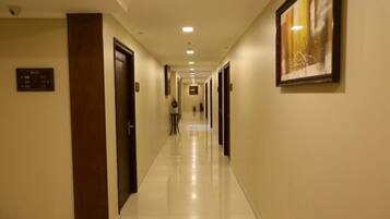 Un pasillo de hotel con puertas a ambos lados, un cartel en la pared izquierda y un cuadro enmarcado a la derecha.