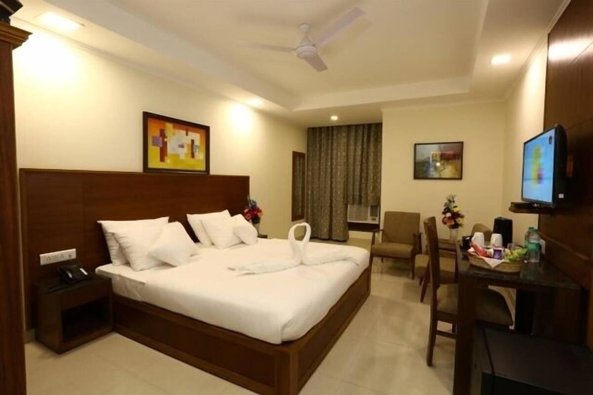 Una habitación de hotel con cama, escritorio, silla, televisor y obras de arte en las paredes.