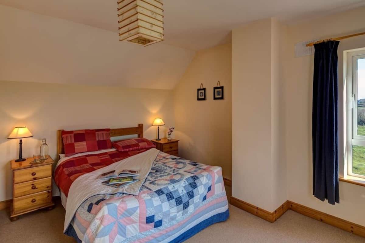 Ein Schlafzimmer mit einem Bett, zwei Nachttischen, einem Fenster mit Vorhängen und einer schrägen Decke.