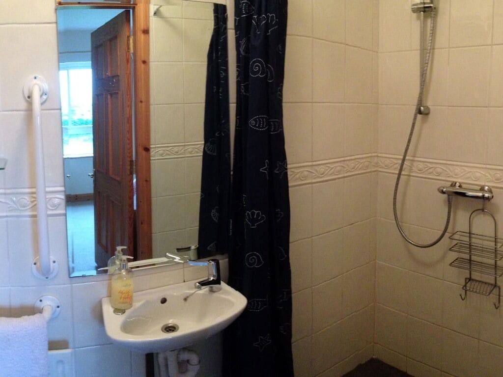 A bathroom with a sink, mirror, shower, and towel rack.