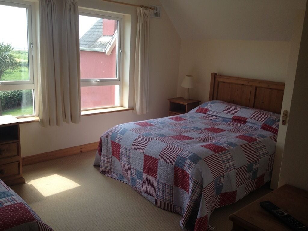 A bedroom with a bed, a nightstand, a window with curtains, and a view of a red building outside.