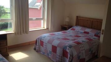 A bedroom with a bed, a nightstand, a window with curtains, and a view of a red building outside.