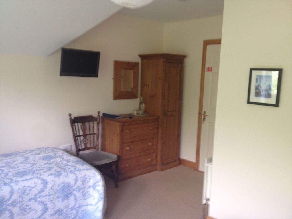 Ein Schlafzimmer mit einem Bett, einer Holzkommode, einem Stuhl, einem an der Wand befestigten Fernseher und einer Tür.