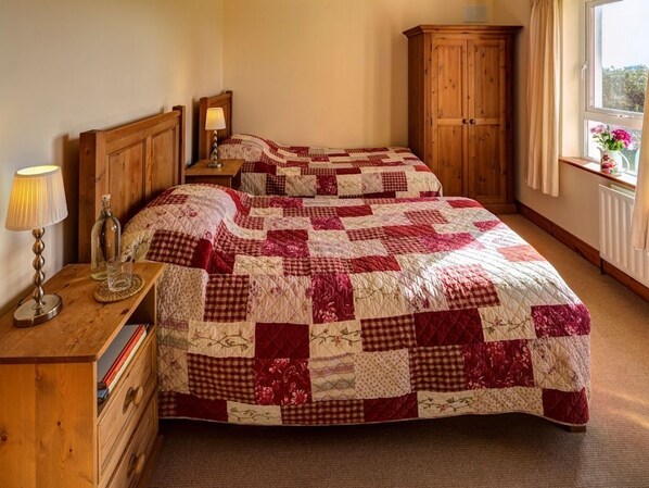 Un dormitorio con dos camas, cabeceros de madera, una mesita de noche con lámpara, un aparador de madera y una ventana con vistas.