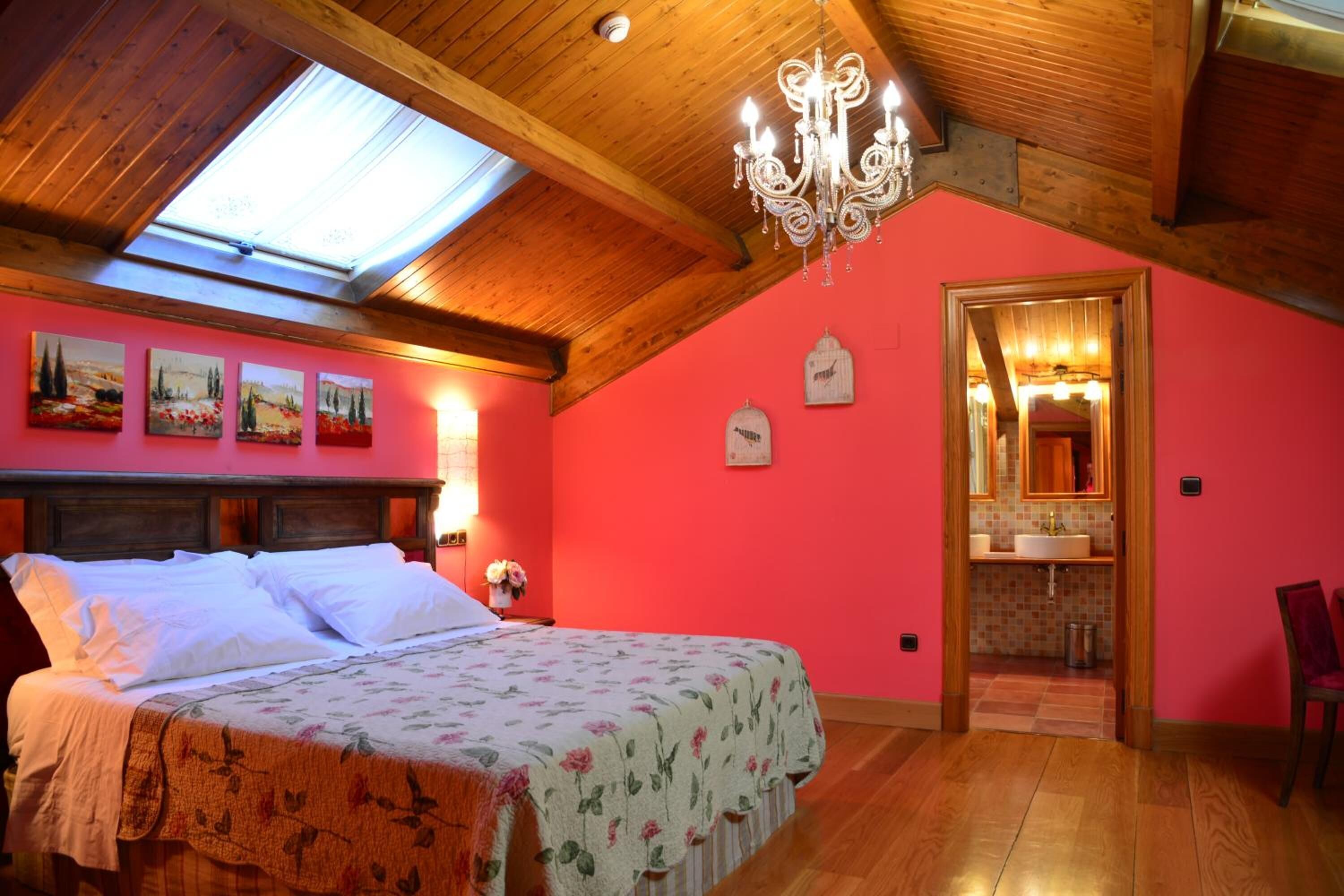 Un dormitorio con techo de madera, tragaluz, candelabro, cama con colcha estampada y pared rosa.