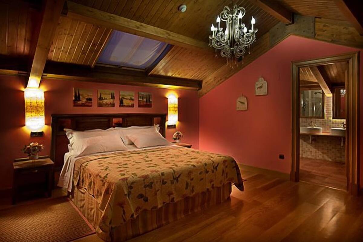 Quarto com teto de madeira, cama com roupa de cama florida, duas luminárias de cabeceira e um claraboia.
