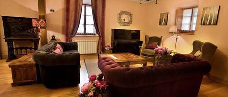 A cozy living room with a fireplace, plush sofas, a piano, and a wooden coffee table.