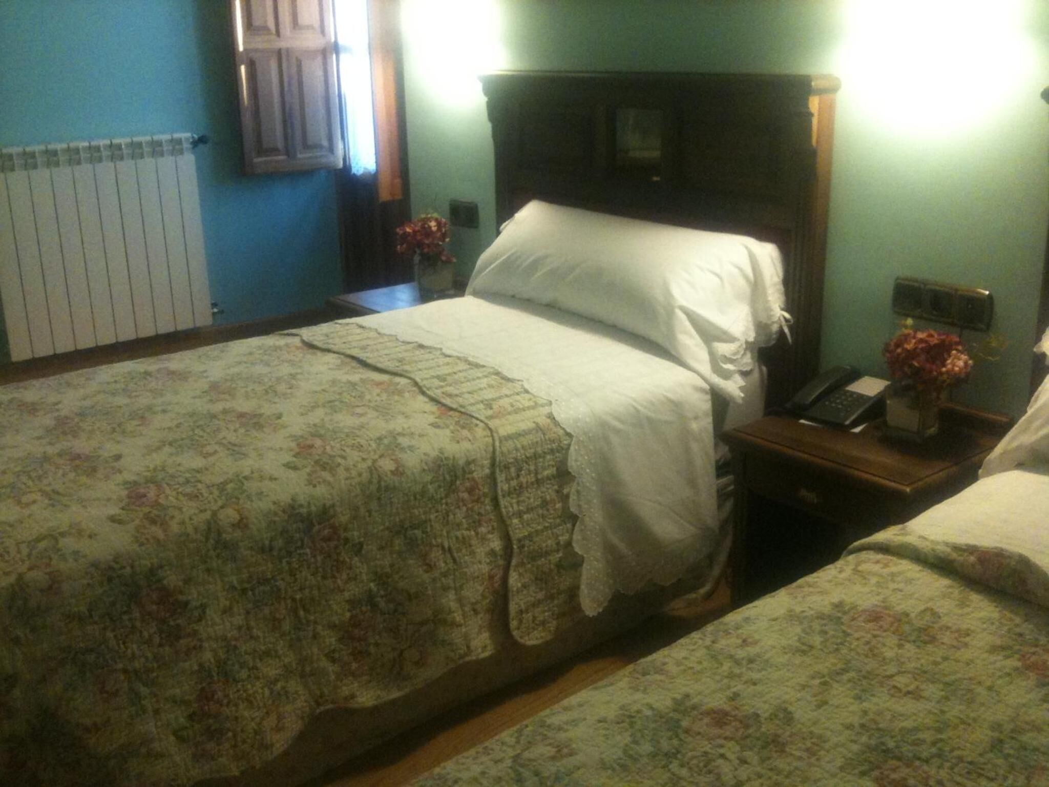 Habitación con dos camas, una mesita de noche con teléfono y un florero, un radiador y una ventana con contraventanas.