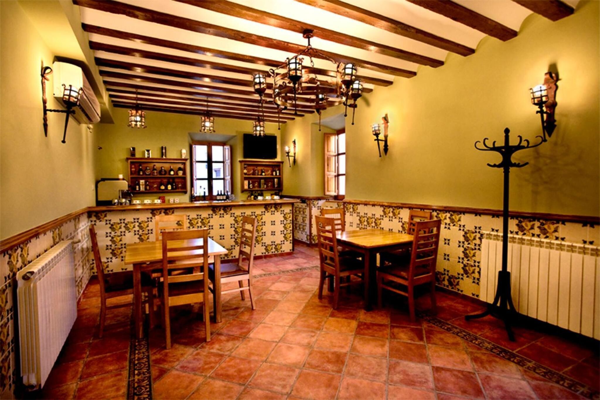 Un comedor con mesas y sillas de madera, suelo de baldosas y techo con vigas a la vista.