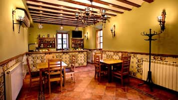 Un comedor con mesas y sillas de madera, suelo de baldosas y techo con vigas a la vista.