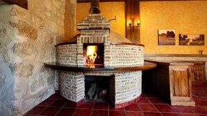 Un horno de ladrillo con leña encendida, situado en un interior rústico con paredes de piedra y vigas de madera.
