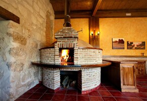 Un horno de ladrillo con leña encendida, situado en un interior rústico con paredes de piedra y vigas de madera.
