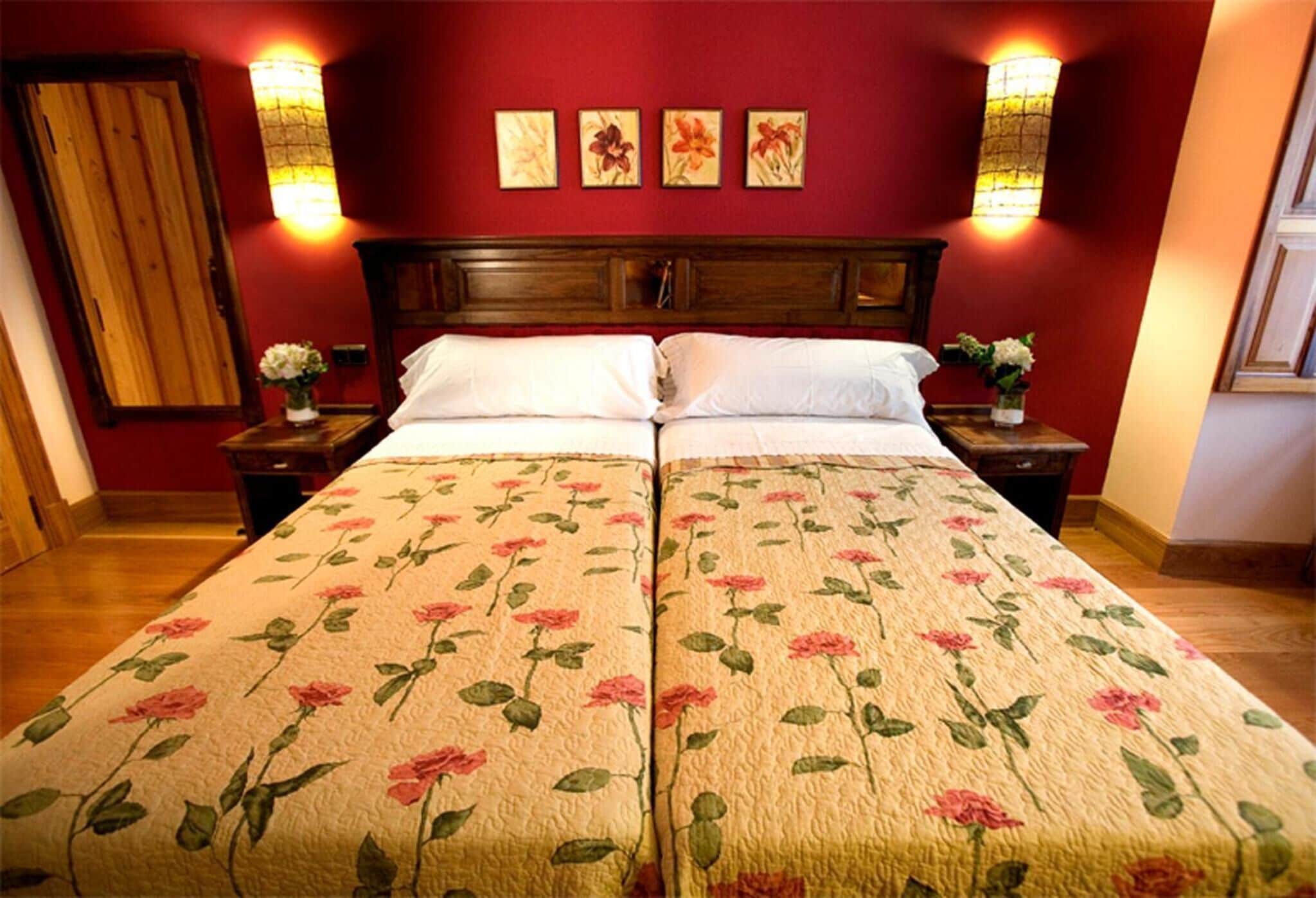 Cama doble con ropa de cama floral, cabecera de madera, lámparas de noche y obra de arte en la pared.