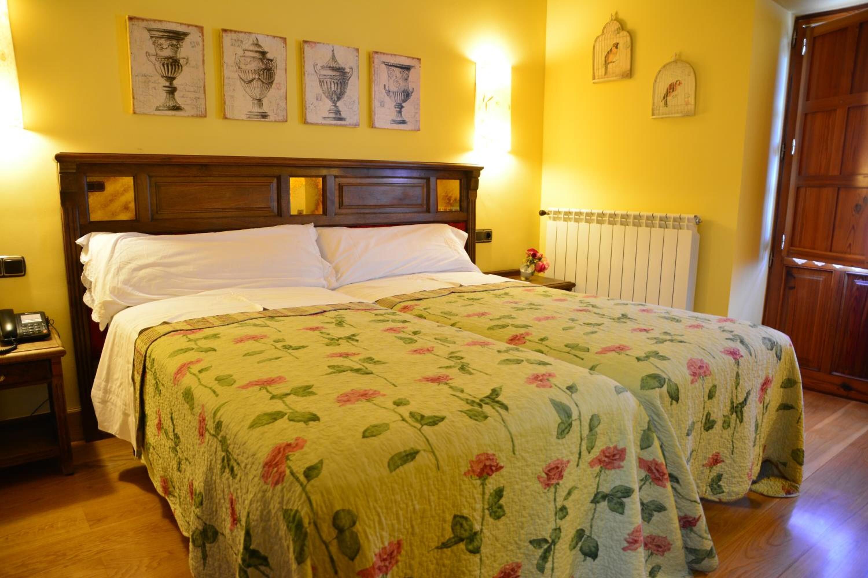 Un lit double avec une literie à motifs floraux, une tête de lit en bois et une table de chevet avec une lampe.