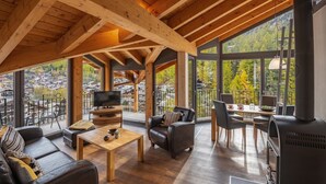Un vaste espace de vie doté d’un plafond haut, de poutres en bois, d’une cheminée, d’un téléviseur et d’un balcon offrant une vue sur la ville et les arbres.
