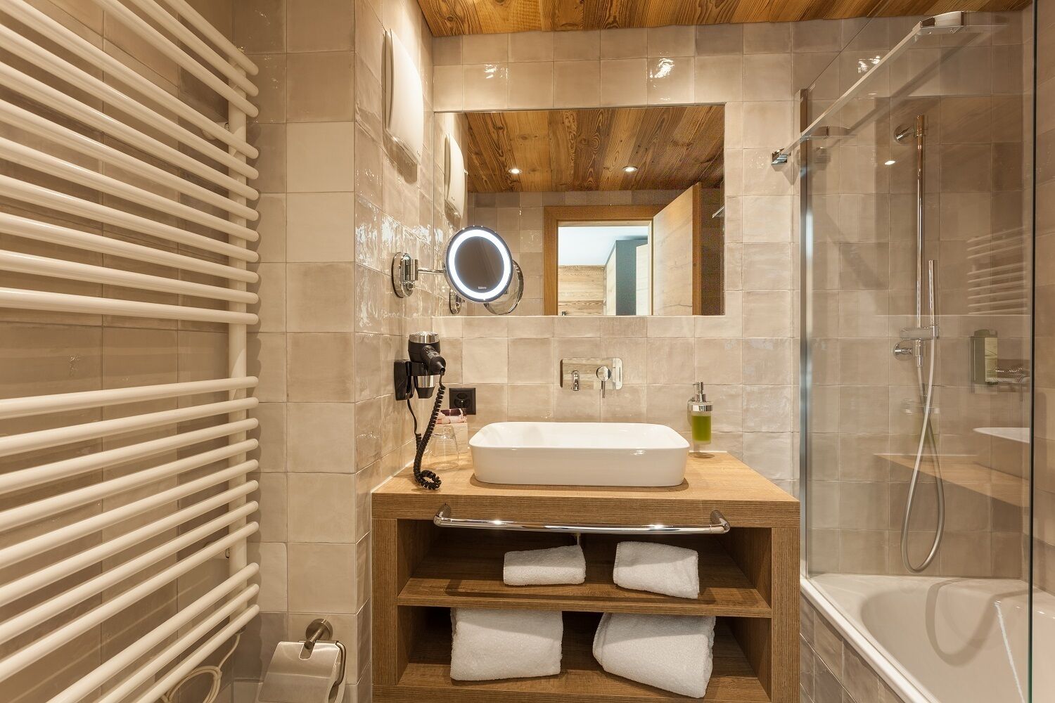 A modern bathroom with a wooden vanity, a large mirror, a built-in shower, and a towel rack.