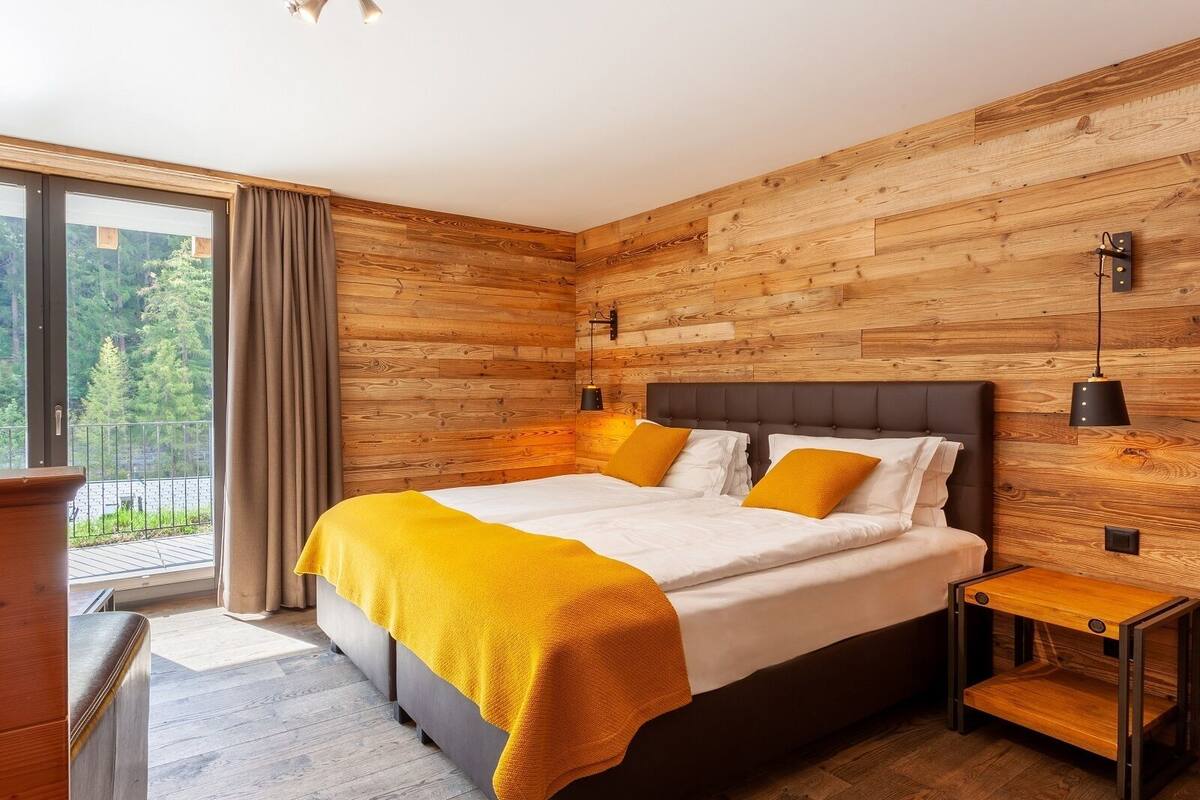 Ein Schlafzimmer mit einem großen Bett, Holzwänden, einem Nachttisch und Blick auf Grünfläche.