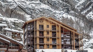 Un immeuble en bois à plusieurs étages, doté de balcons, entouré de montagnes enneigées.