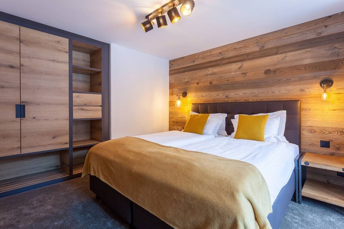 Ein modernes Schlafzimmer mit Holz-Kopfteil, einem Bett mit weißen Leinen und gelben Kissen, einem eingebauten Kleiderschrank und Wandleuchten.