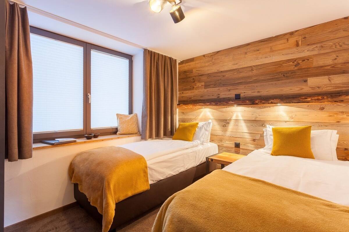 Ein Hotelzimmer mit zwei Betten, Holzwandverkleidung, einem Fenster mit Vorhängen und einem Nachttisch mit Lampe.