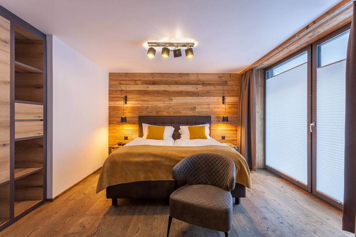 Ein modernes Schlafzimmer mit einem Holzkopfende, einem großen Bett mit gelbem Akzentkissen, einem Nachttisch mit Lampe und einem Sessel.