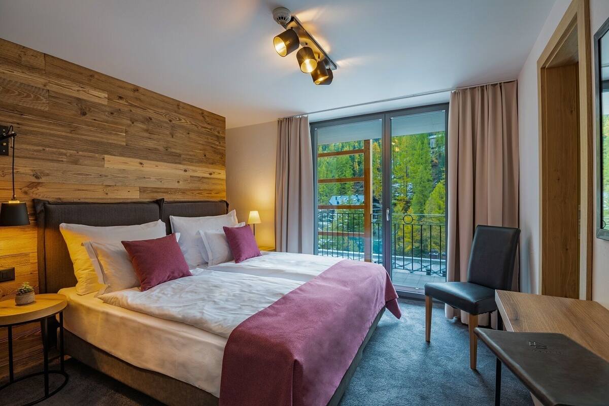 Ein modernes Hotelzimmer mit einem großen Bett, einem Schreibtisch und einem Balkon mit Blick auf Bäume.