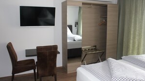 Ein Hotelzimmer mit Bett, Stuhl, Fernseher, Kleiderschrank und Spiegel.