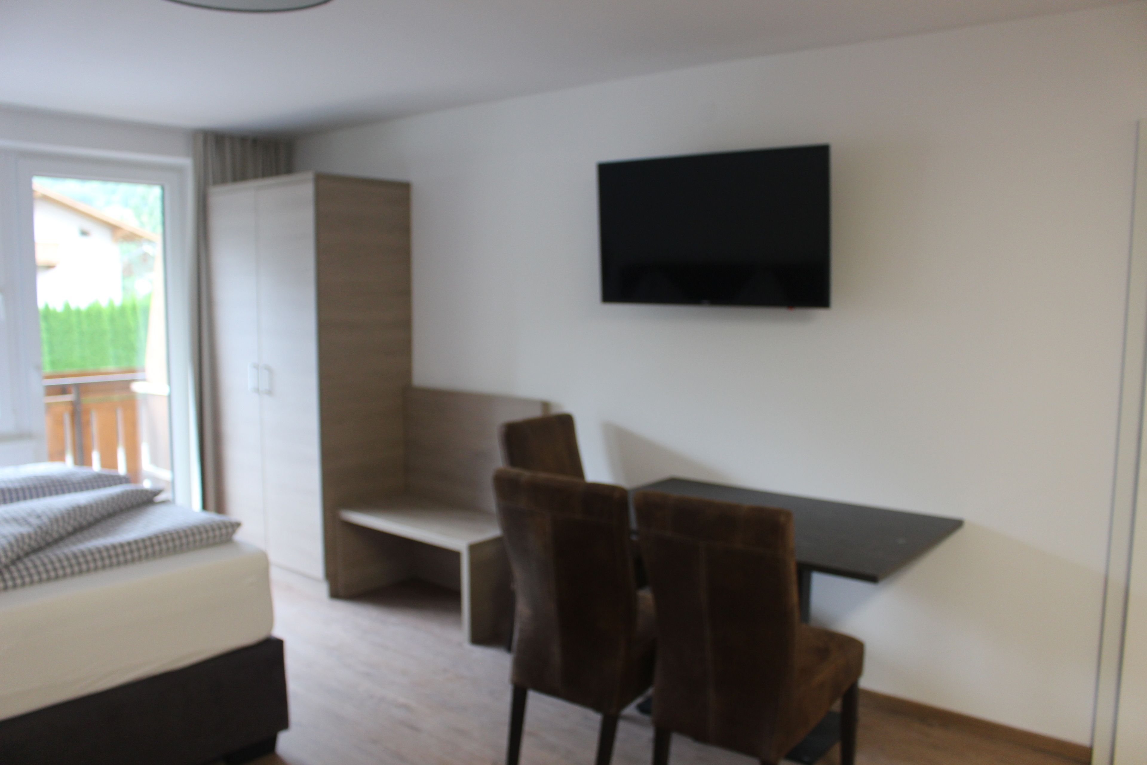 Quarto moderno com cama, escrivaninha e televisão fixada na parede.