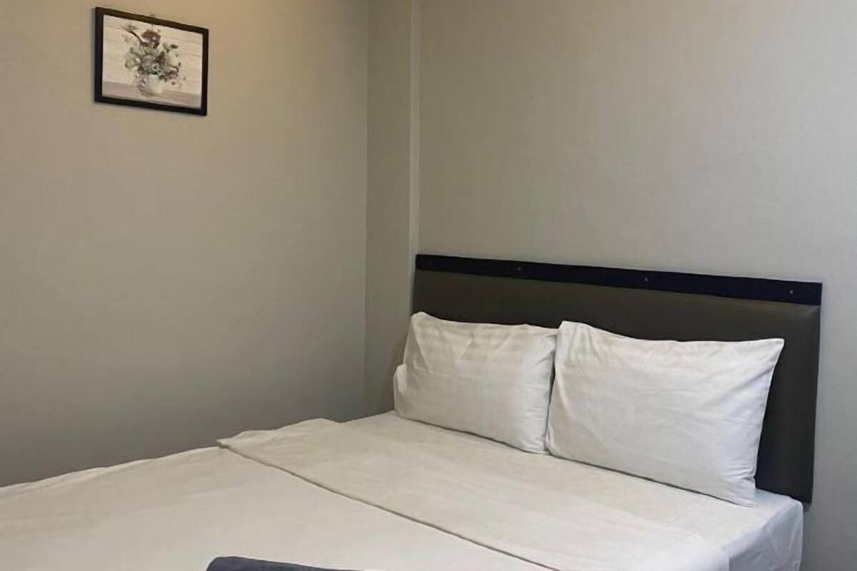 Un lit simple avec une tête de lit sombre et du linge de lit blanc, dans une pièce aux murs de couleur neutre.